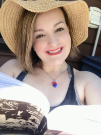 A woman wearing a beige hat is smiling from behind an open book.